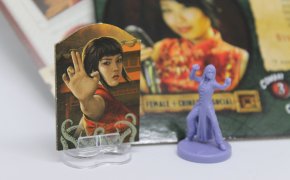 Standee di Eldritch Horror a sinistra e miniatura di Fortune and Glory: the Cliffhanger Game a destra.